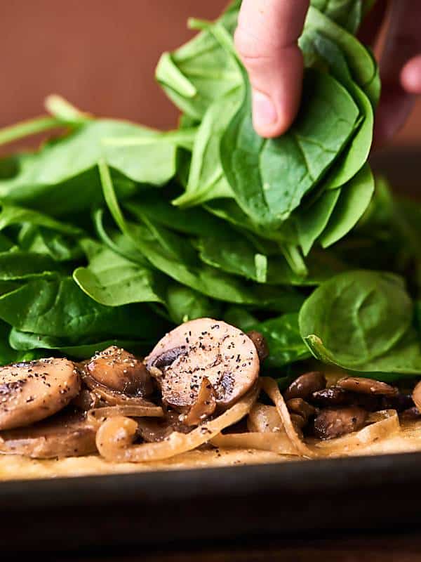 Fresh spinach being put on pizza