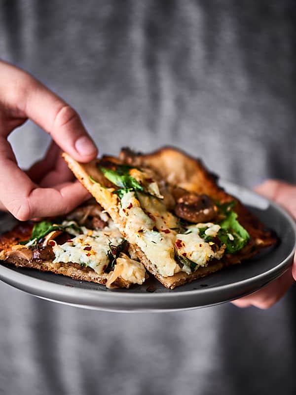 Two slices of caramelized onion and mushroom pizza on a plate held