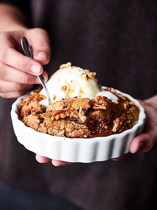 Bowl of slow cooker caramel apple dump cake with ice cream held