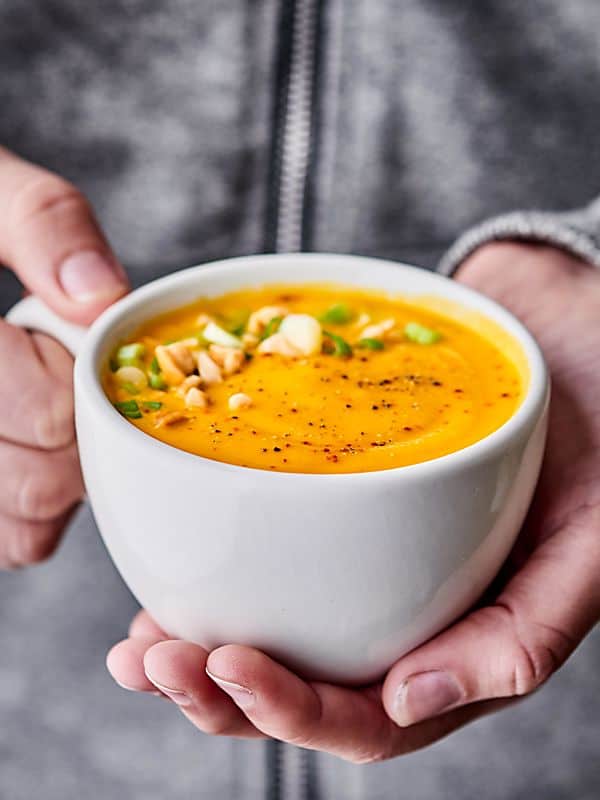 Mug with roasted carrot soup held two hands