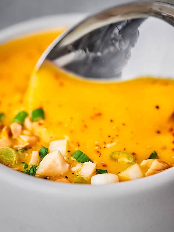 Closeup of carrot soup with spoon being dipped 