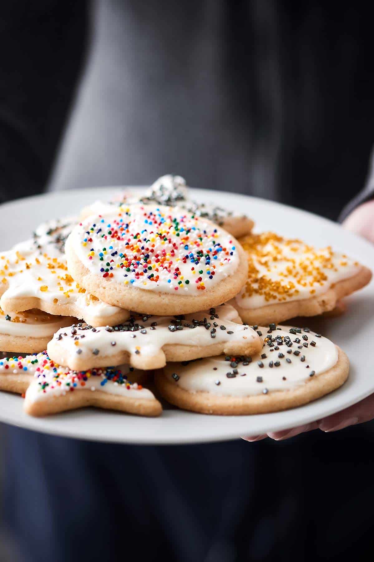 Cut out sugar cookies with cream cheese frosting on plate held