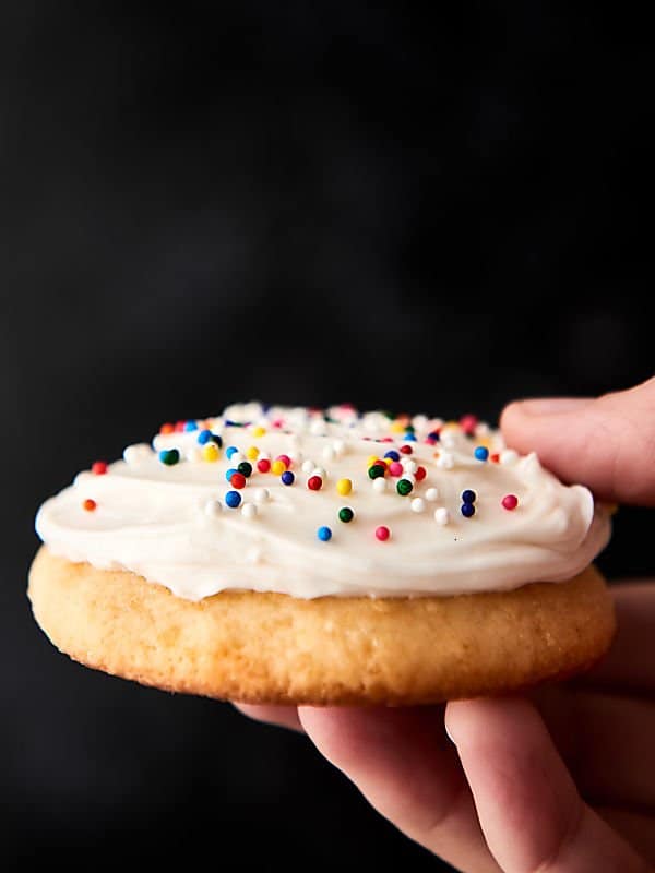 Frosted sugar cookie with sprinkles held