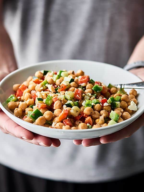 plate of chopped chickpea greek salad held two hands