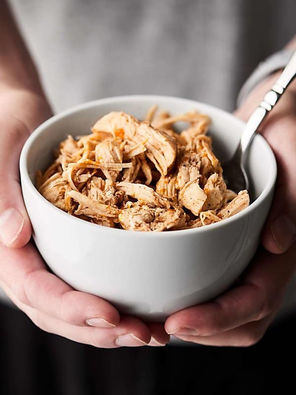 Bowl of instant pot shredded chicken with fork held