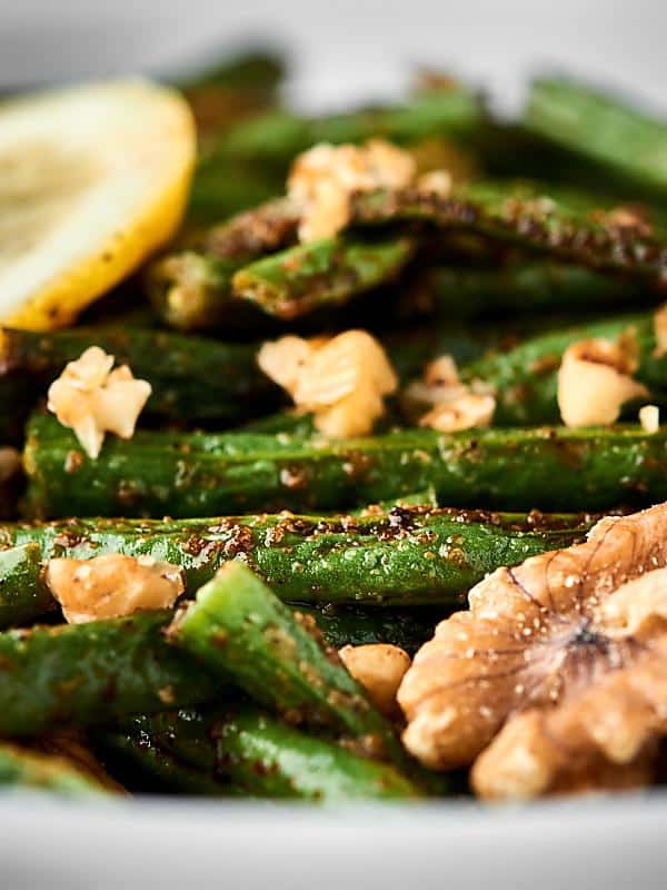 Up close roasted green beans with walnuts and lemon slice