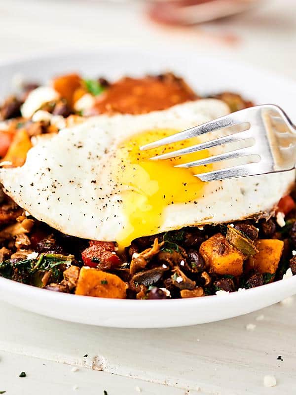 Closeup runny fried egg being cut with fork on breakfast burrito bowl