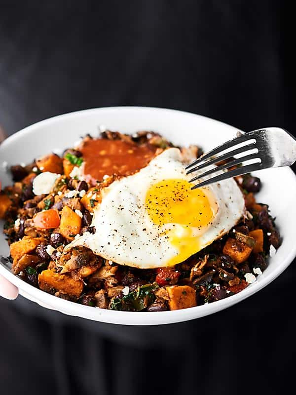 This Breakfast Burrito Bowl Recipe is full of sweet potatoes, peppers, onion, spinach, mushrooms, garlic, black beans, and spices. Topped with a fried egg, salsa, and greek yogurt! Healthy. Meatless. Gluten Free. Perfect for meal prep! Can be vegan! showmetheyummy.com #breakfast #healthy #burrito