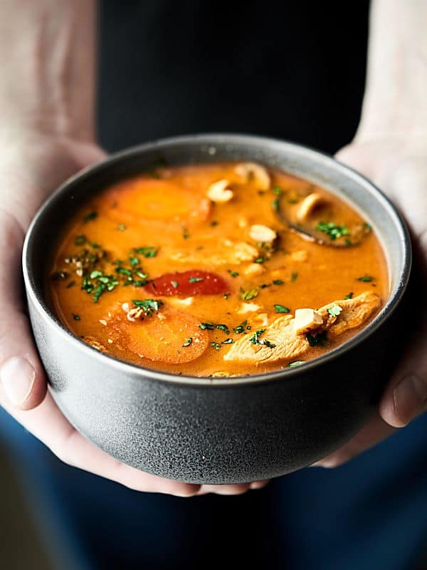 Bowl of thai chicken soup held in two hands