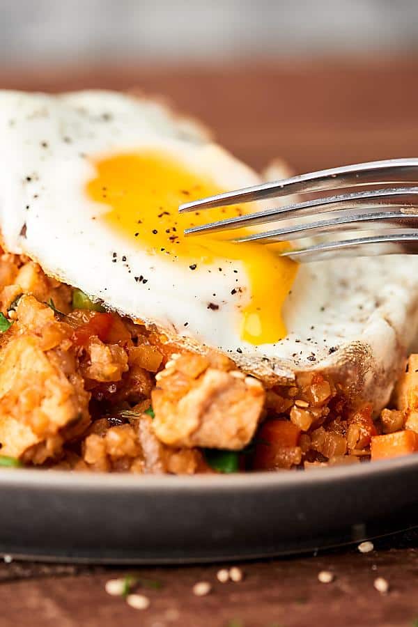 fried egg being cut on plate of chicken cauliflower fried rice