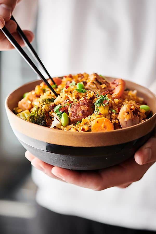 Pork fried rice in a bowl held with chopsticks