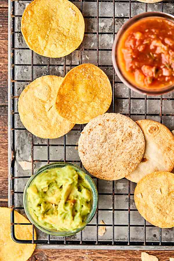 Air fryer tortilla chips on cooling rack with guac and salsa above