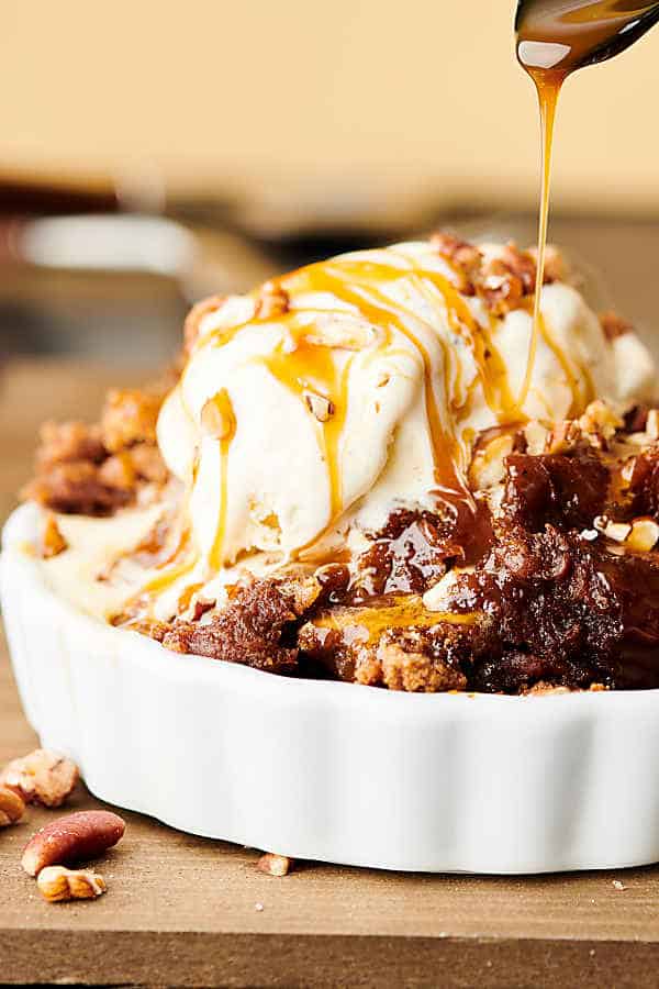 crockpot pumpkin dump cake in bowl, caramel being drizzled