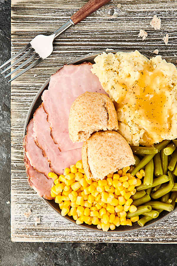 plate of ham, mashed potatoes, corn, beans, and bread above