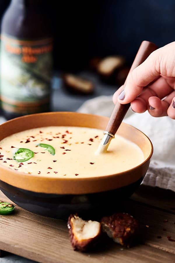 Spoonful being taken out of bowl of soup with pretzel bites sitting in front and bottle of beer in the background