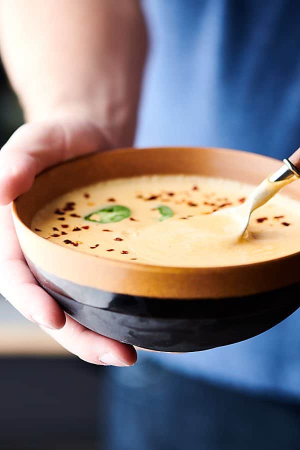 Bowl of beer cheese soup garnished with jalapeño and red pepper flakes being held