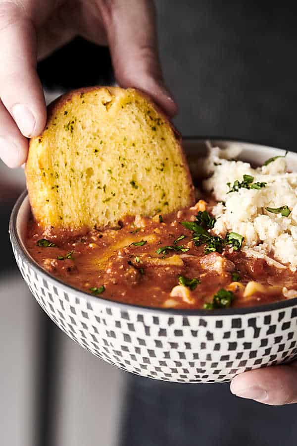 piece of garlic bread being dipped into bowl of lasagna soup