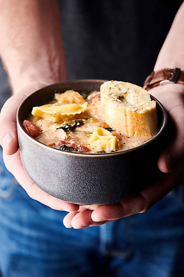 Bowl of chicken tortellini soup held two hands