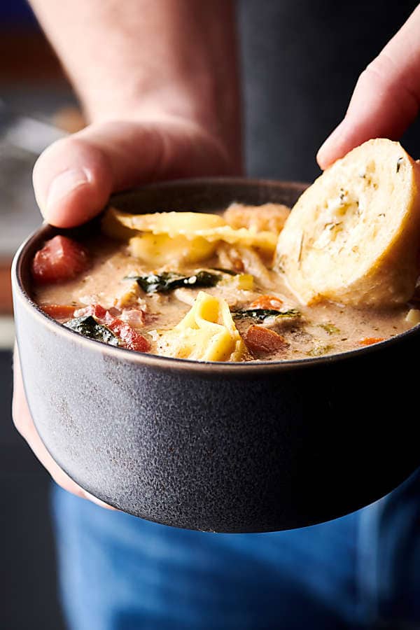 Chicken tortellini soup in bowl with slice of bread held 