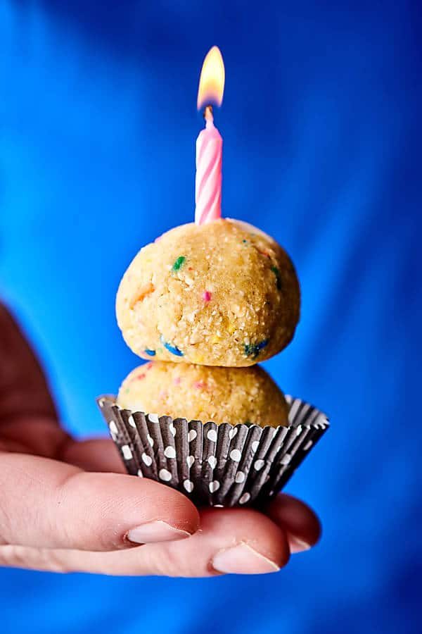 funfetti cookie dough balls stacked in muffin wrapper, held, with lit candle