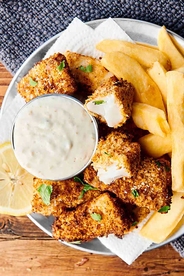 Homemade healthy air fryer fish sticks on plate with fries and dressing above