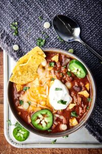 This Instant Pot Chili Recipe is SO quick, easy, and loaded with bacon, beef, beer (optional), broth, tomato sauce, veggies, beans, and spices! Serve with optional, but highly recommended cornbread, shredded cheese, and sour cream! SO hearty and cozy. showmetheyummy.com #instantpot #beef #chili
