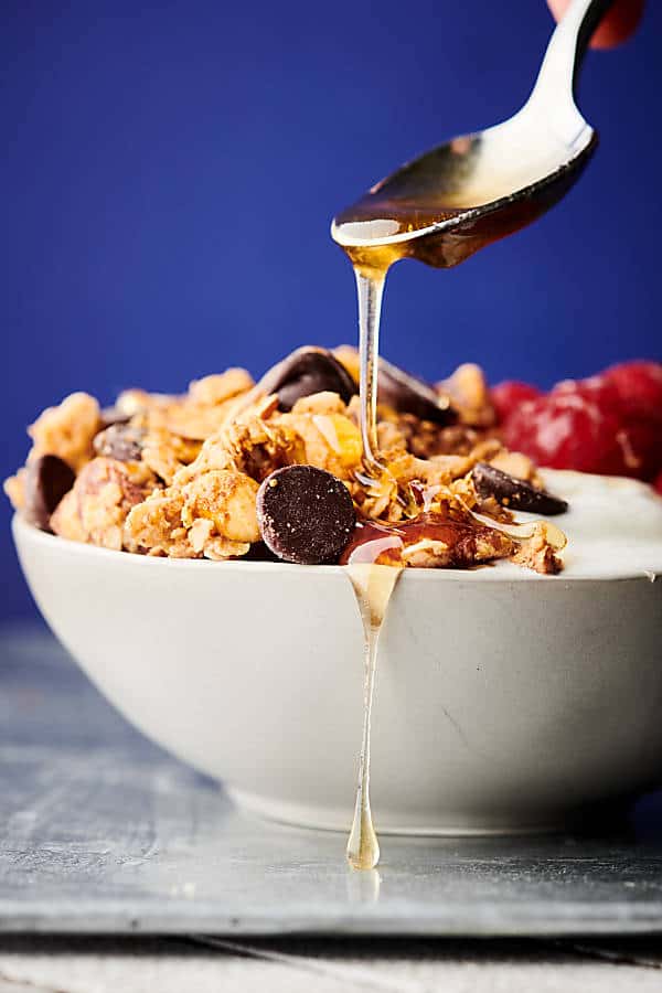 bowl of almond butter granola, honey being drizzled on top with spoon