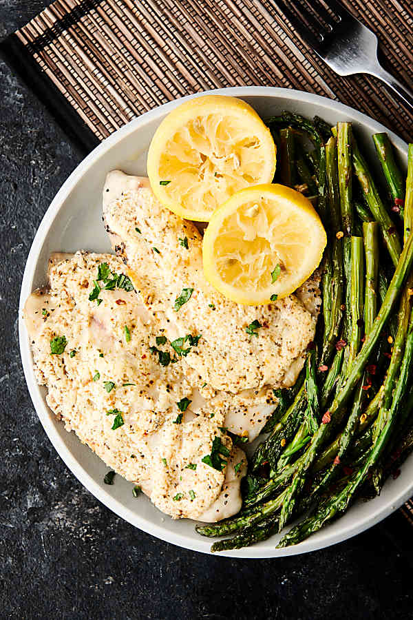 Healthy greek yogurt lemon parmesan tilapia with lemon and asparagus on plate above