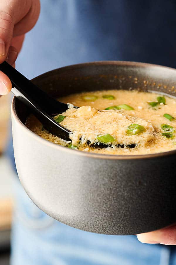 bowl of egg drop soup held, spoon being lifted out