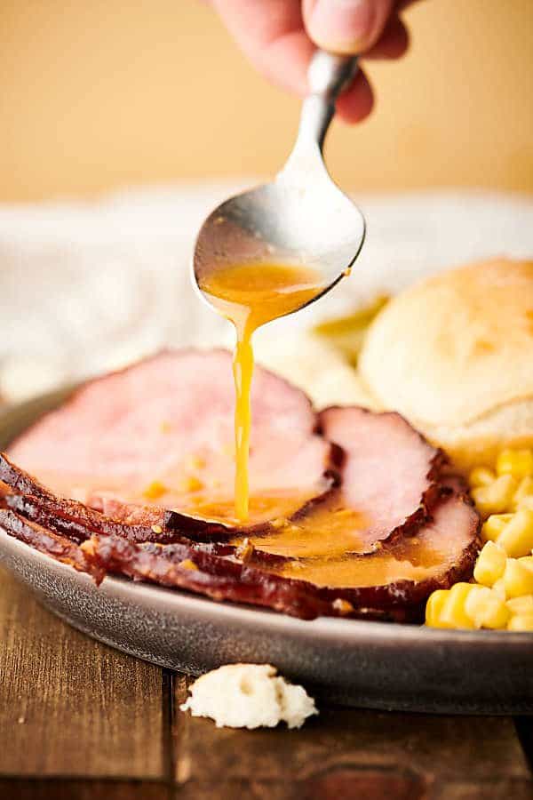 sauce being drizzled over sliced ham on plate