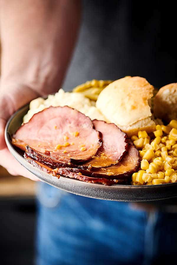 honey dijon crockpot ham sliced on plate with sides held two hands