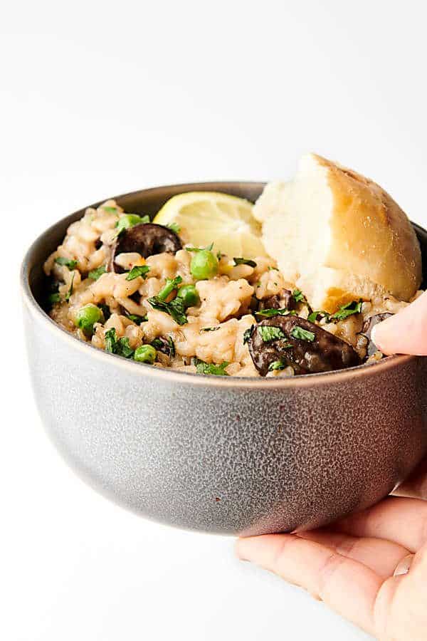 Bowl of risotto with bread and lemon wedge held one hand