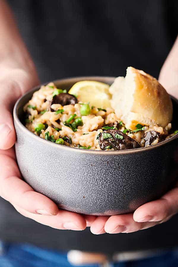 Bowl of instant pot mushroom risotto with bread and lemon wedge held