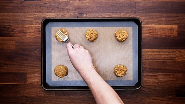 Fork being used to make indents in peanut butter oatmeal cookies on baking sheet