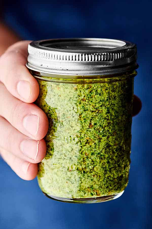 jar of homemade basil pesto held blue background