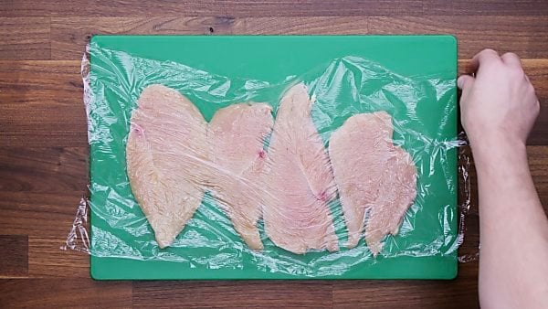 Cut and pounded chicken breasts covered in plastic wrap