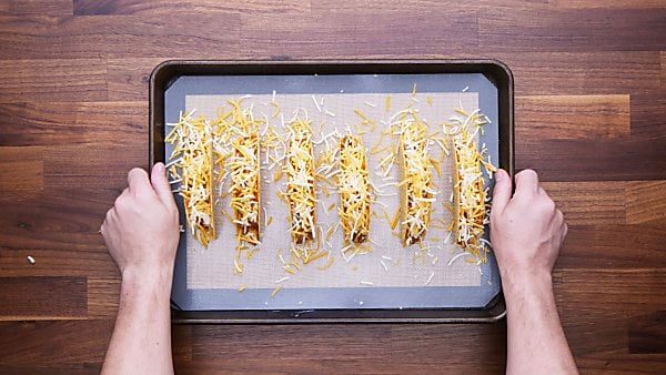 Tacos with filling and more cheese on baking sheet