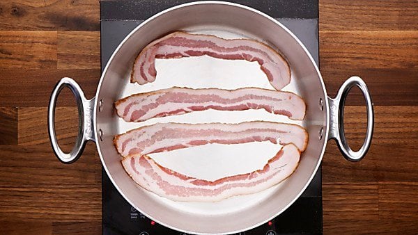 four strips of bacon being cooked in skillet