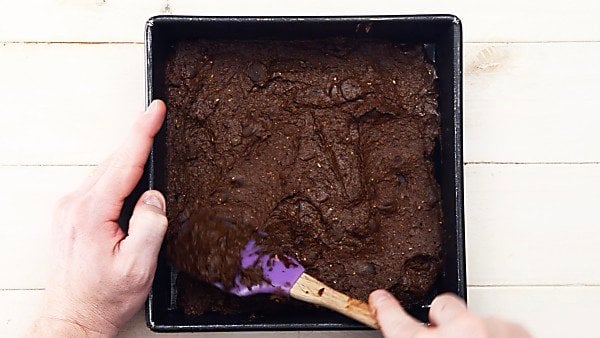 brownie batter being spread into baking pan with spatula