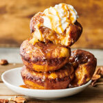 Stack of 3 caramel apple pie dumplings on a plate with ice cream and caramel drizzle
