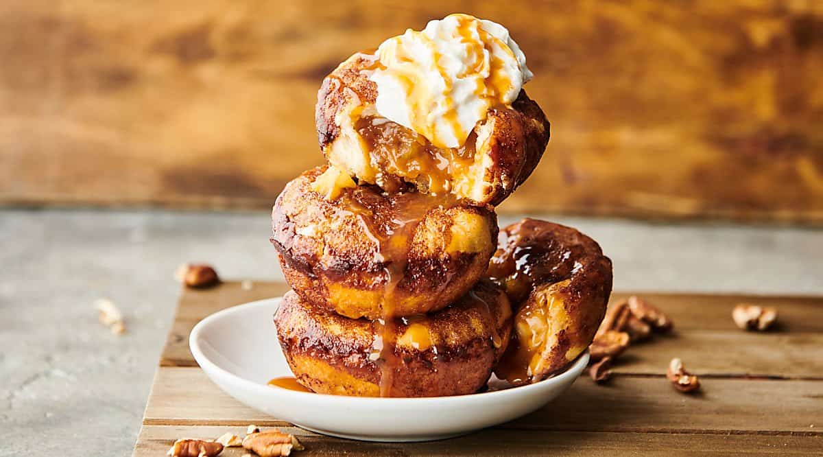 Stack of 3 caramel apple pie dumplings on a plate with ice cream and caramel drizzle