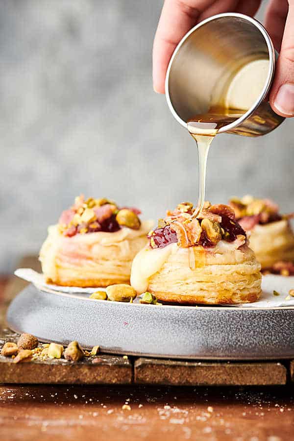 Honey being drizzled over plate of cranberry brie bites.