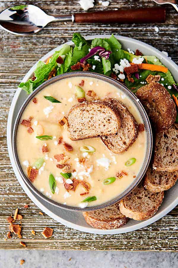 Overhead shot of bowl of instant pot potato soup with garnishes on a plate with bread and salad