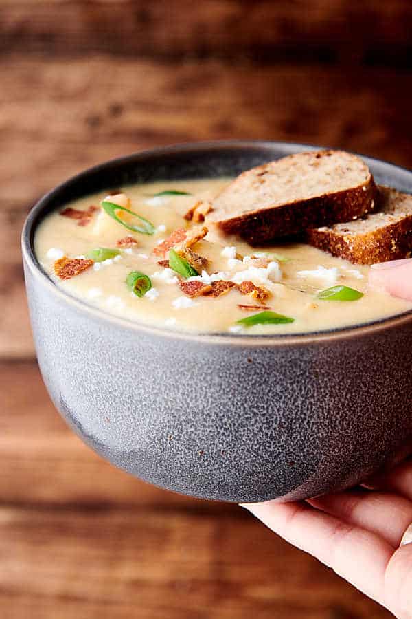 Bowl of instant pot potato soup with garnishes and two slices of bread being held