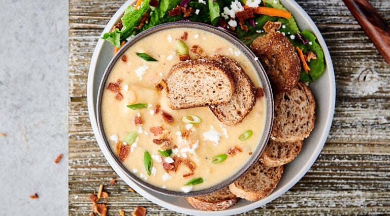 Overhead shot of bowl of instant pot potato soup with two bread slices on a plate with salad and more bread