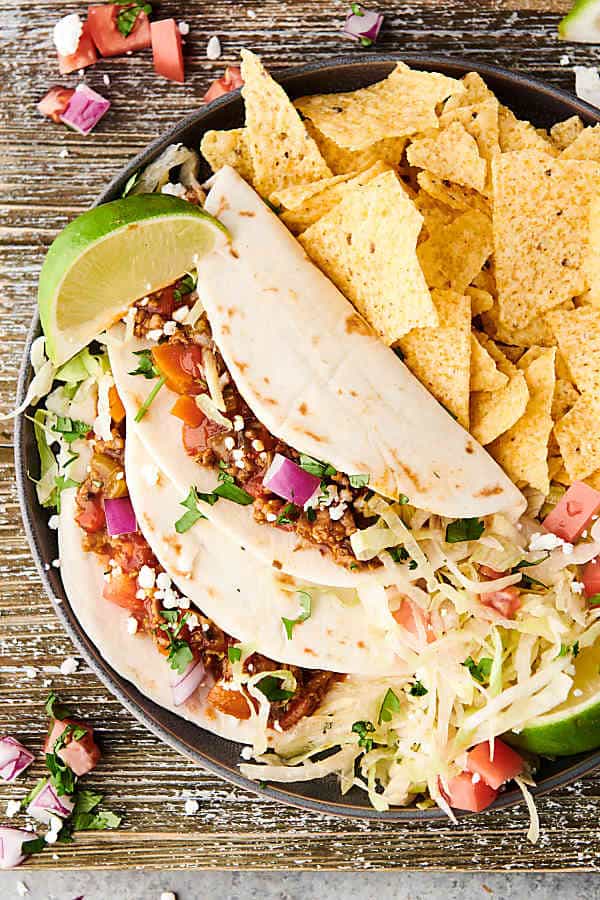 Two instant pot turkey tacos on a plate with tortilla chips and lime taken from above