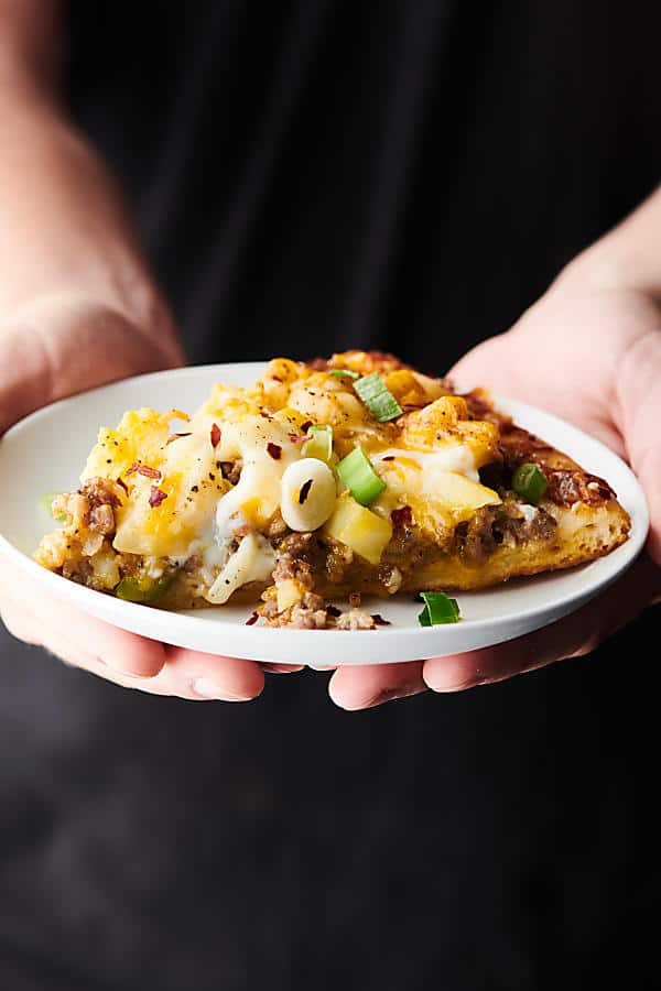 Slice of maple sausage breakfast pizza on a plate being held