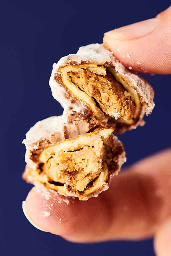 Close-up of two peanut butter pretzels with chocolate and powdered sugar coating being held