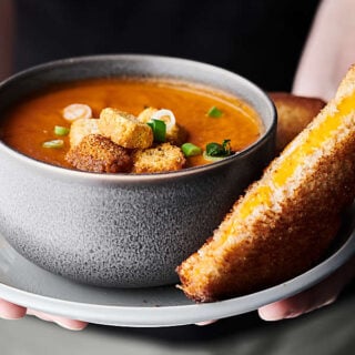 Bowl of roasted tomato soup on a plate with grilled cheese sandwich