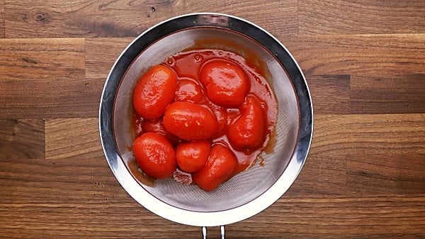 Canned tomatoes being drained in sieve